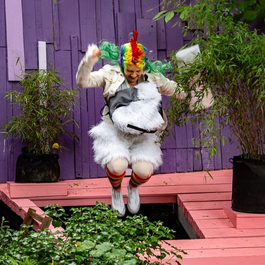 Ein Schauspieler, der als Einhorn verkleidet ist, springt auf einer pinken Bühne in die Luft