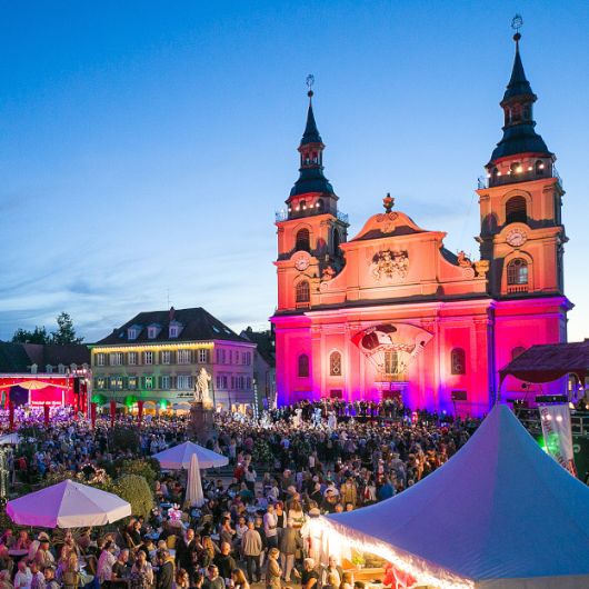 Zu sehen ist die beleuchtete evangelische Stadtkirche sowie ein großes Publikum davor.