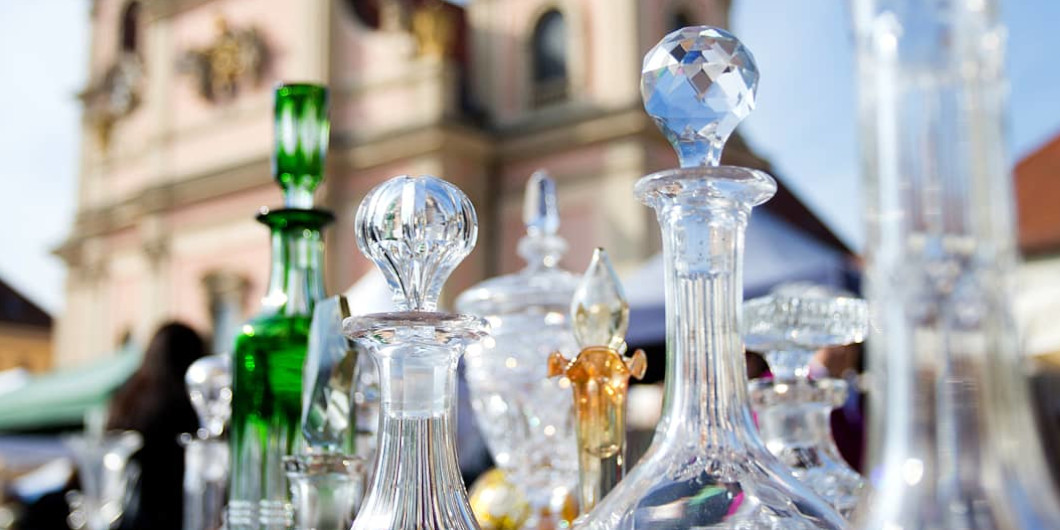 Im Vordergrund sieht man alte Glaskaraffen und -gefäße, im Hintergrund die evangelische Stadtkirche Ludwigsburg