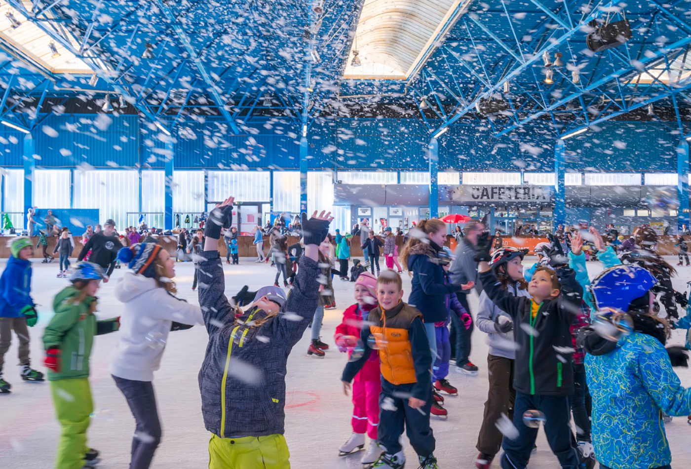 Kinder mit Schneeanzügen auf der Eisbahn versuchen Kunstschneeflocken einzufangen.