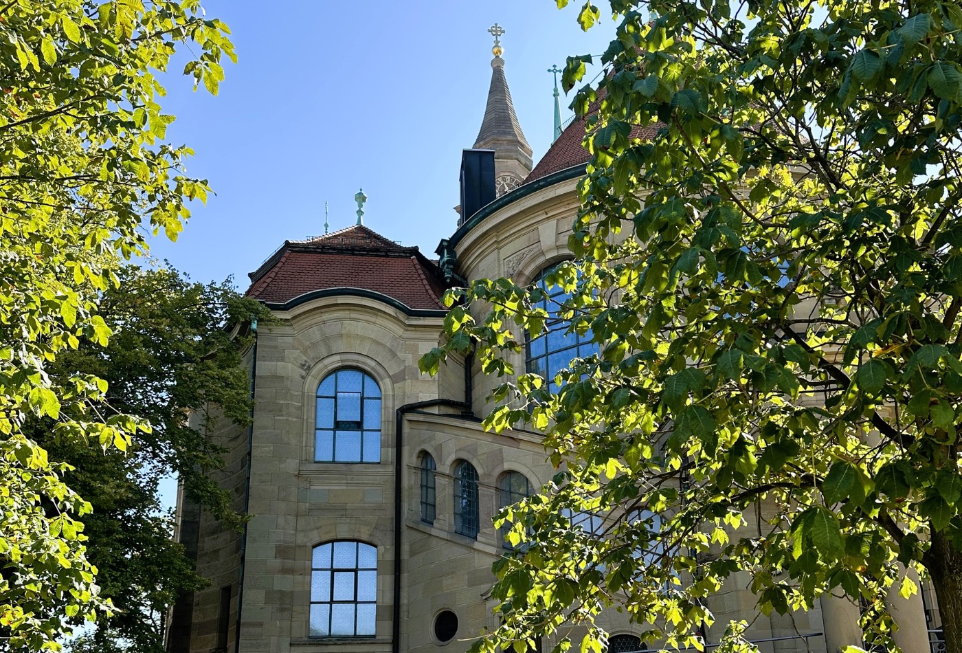 die Friedenskirche, halb verdeckt von sonnenbeleuchteten Blättern zweier Bäume