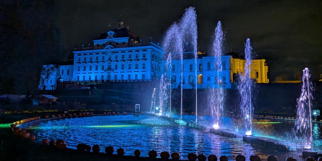 Die Fassade des Residenzschlosses ist blau beleuchtet, im Vordergrund ein ebenfalls blau beleuchtetes Wasserspiele