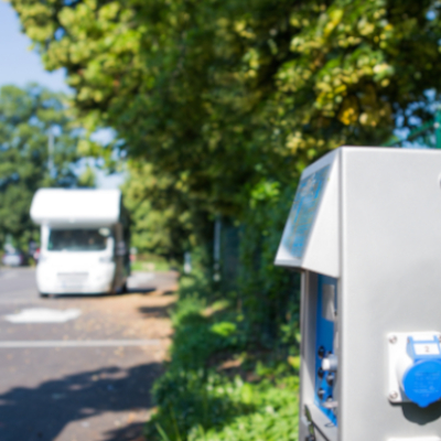 Ein Wohnmobil steht auf einem Wohnmobilstellplatz im Hintergrund, im Vordergrund sieht man eine Ladestation