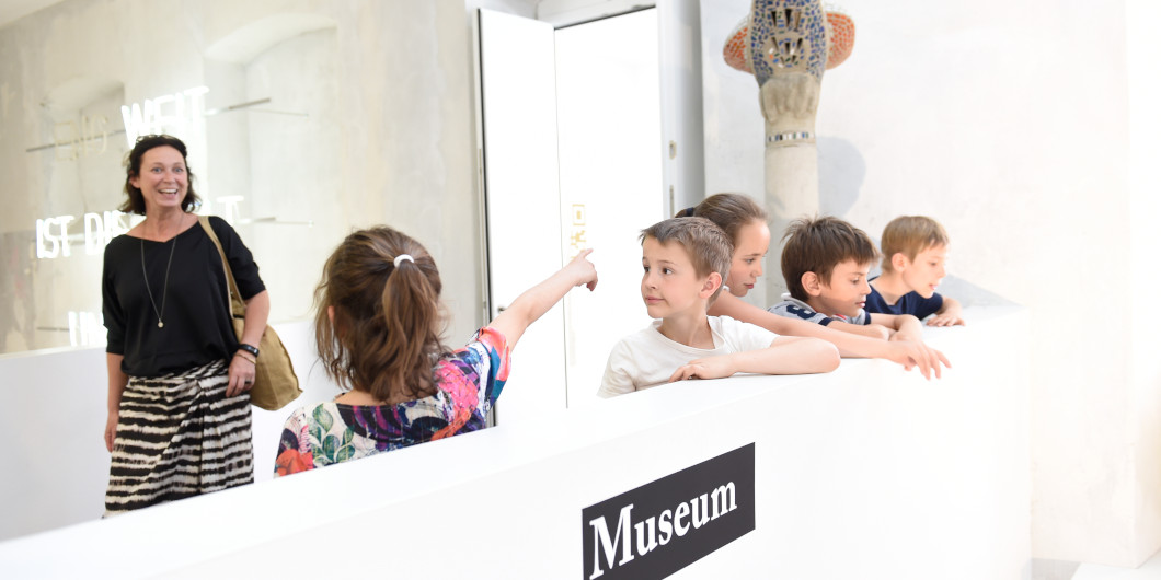 Vier Kinder sind mit einer erwachsenen Person im Museum und schauen sich die Exponate an.