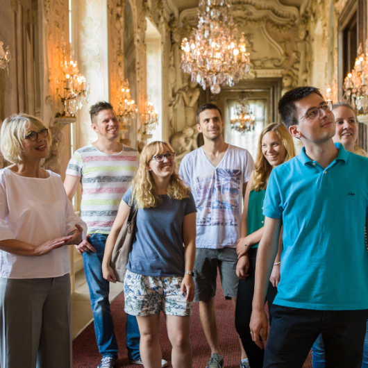Zu sehen ist eine Gruppe Touristen, die sich die Inneneinrichtung des Residenzschlosses ansieht.