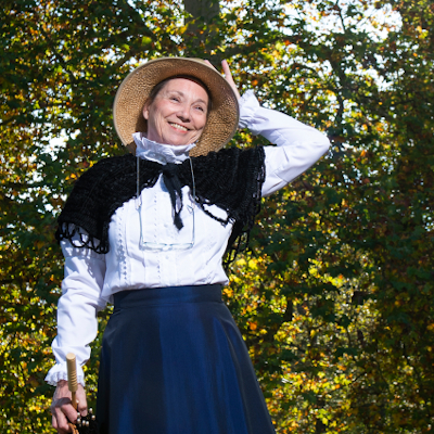 Eine Frau blickt freudig in die Kamera, sie trägt Kleidung von 1900.