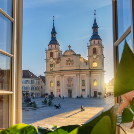 Zu sehen ist der Blick auf die Evangelische Stadtkirche sowie den Markplatz von einem Fenster aus.